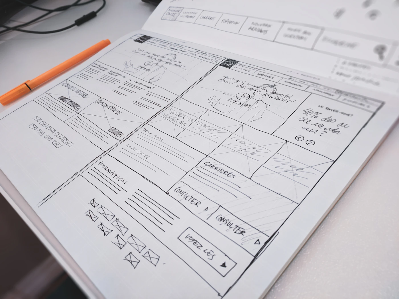 A website layout sketched on paper beside an orange pen